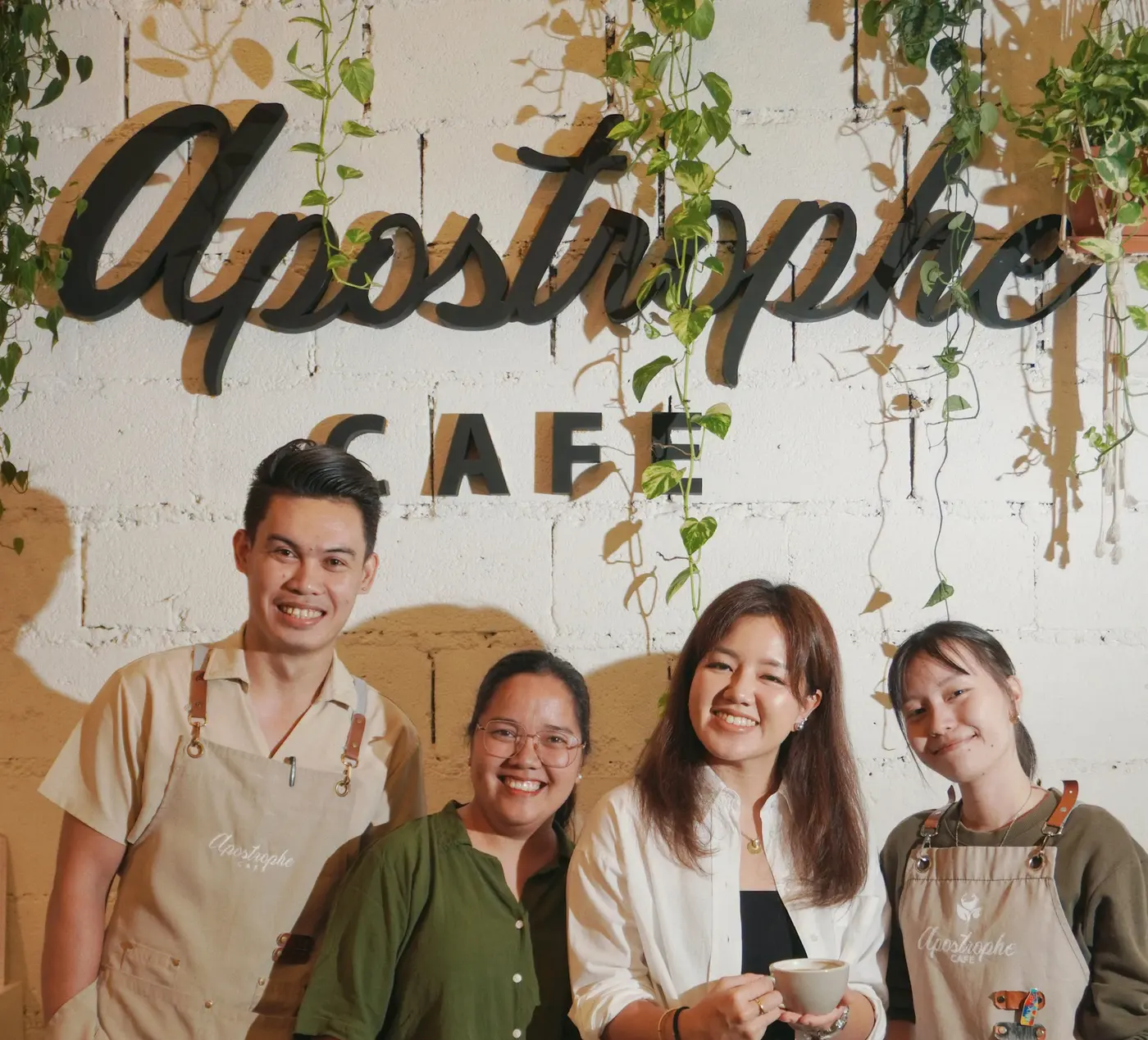 The Apostrophe Cafe team smiling under the cafe's script sign